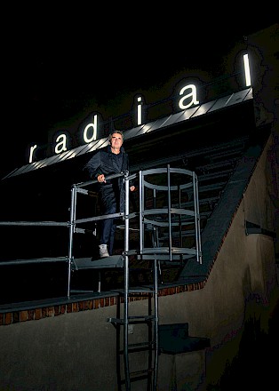 Mischa Kuball steht auf einer Feuertreppe auf dem Dach des Radialsystems. Hinter ihm die Leuchtschrift