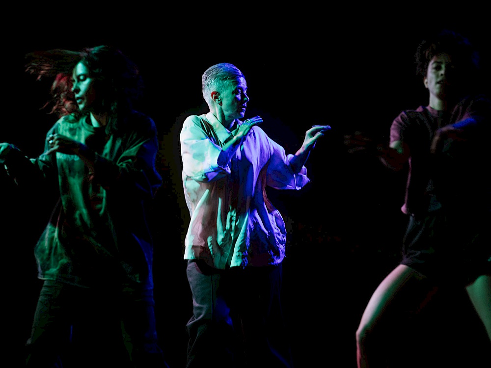 Three dancers in dynamic poses against a dark background