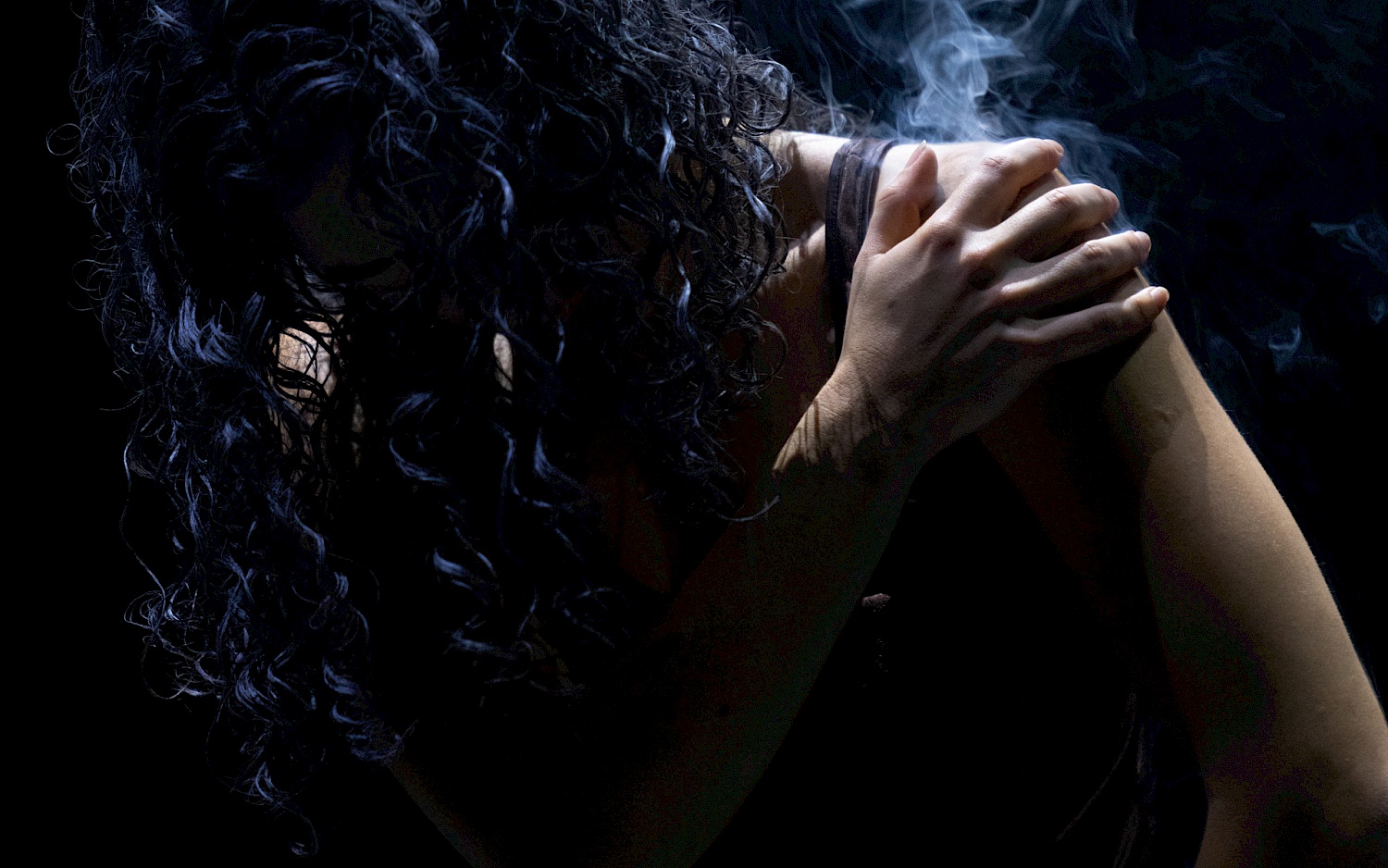 Dinis Santos A person with long black curled hair touches their shoulder with their hand. The affected area is smoking.