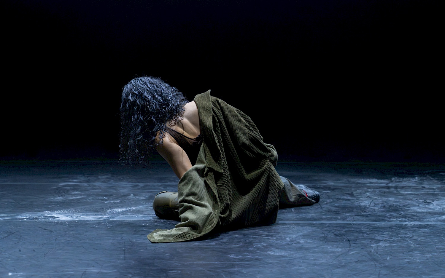 Dinis Santos A person with black curly hair is sitting with their back to the viewer. Their upper body is leaning slightly to the left.