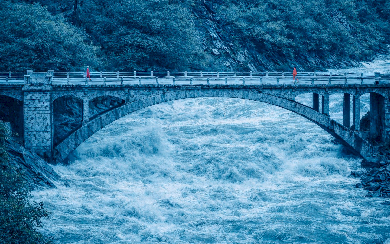 NICO AND THE NAVIGATORS Zwei Personen gehen auf einer Brücken aufeinander zu, die über einen reißenden Fluss führt.