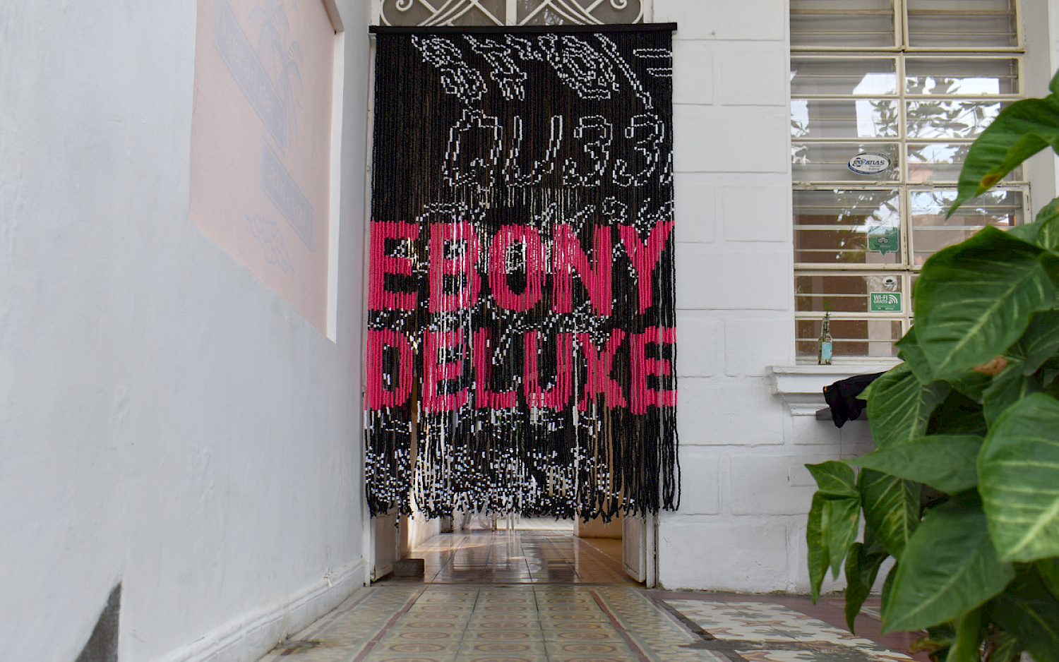 Laura Campaz Perlenvorhang mit der Aufschrift „EBONY DELUXE“ in einem Flur mit Pflanzen und gefliestem Boden