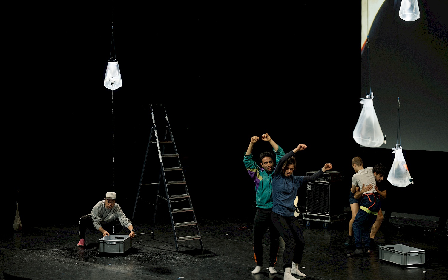 Five people perform on stage. Transparent bags filled with water hang from the ceiling.