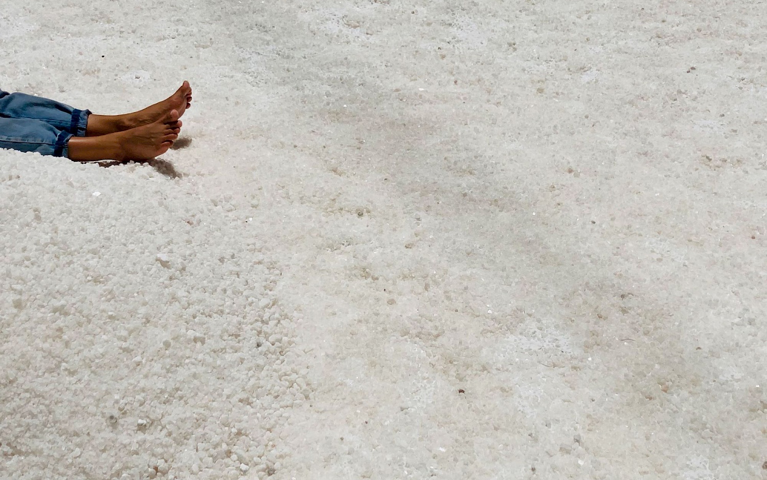 A pair of bare feet protrude into the picture from the left edge. The ground is completely covered with salt.