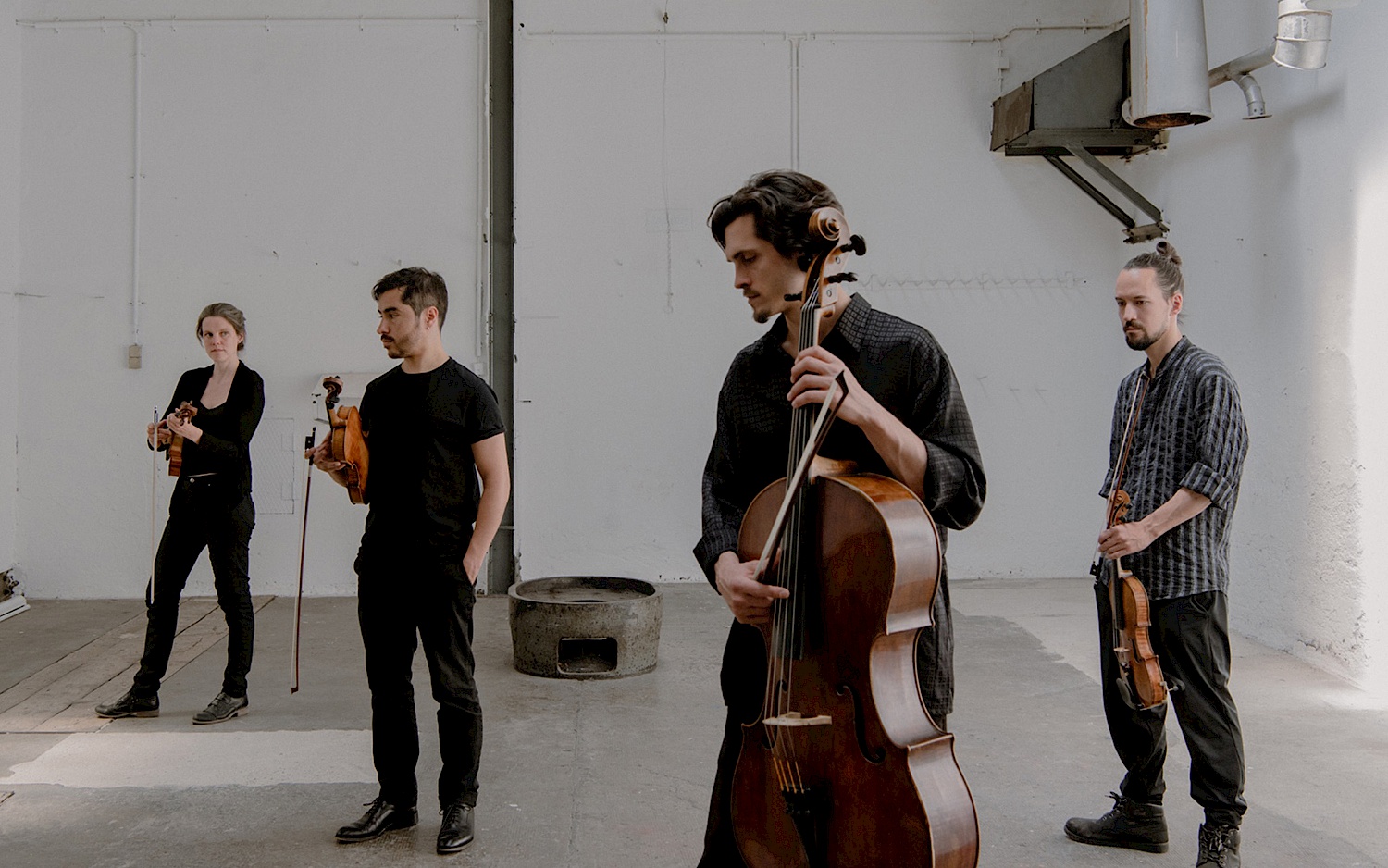 Das Paranormal String Quartet steht mit ihren Instrumenten, Felix Key Weber und Gustavo Strauß mit Violine, Katherine Barritt mit Viola und Jakob Roters mit Violoncelle in einem industriell wirkenden Raum in größeren Abständen