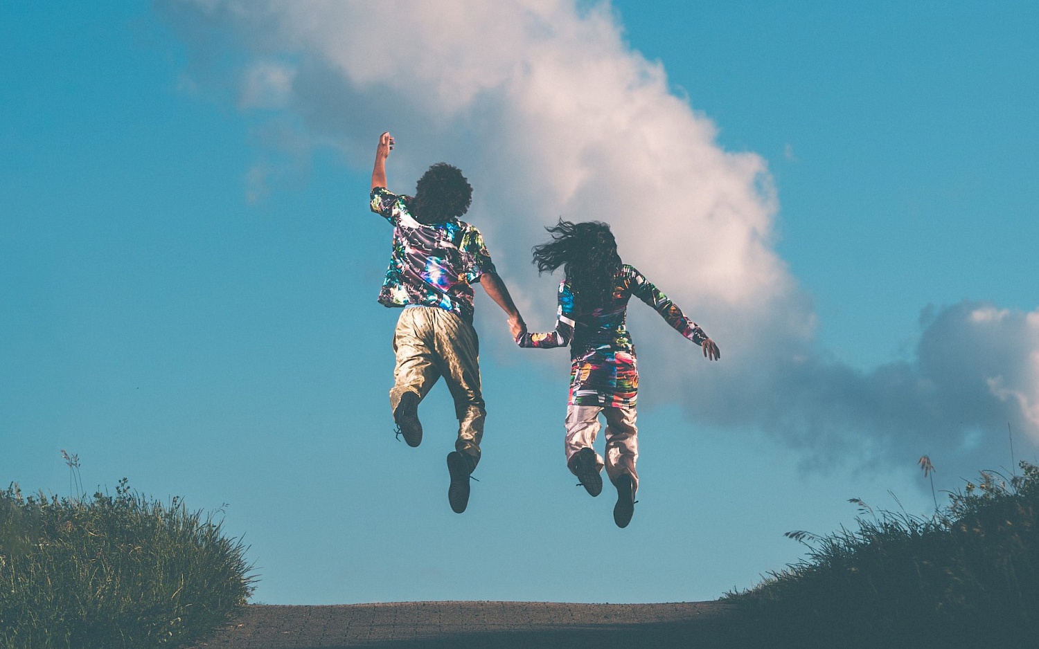 Raphael Moussa Hillebrand und Joy Alpuerto Ritter fliegen Hände haltend von der Erde Richtung blauen Himmel.