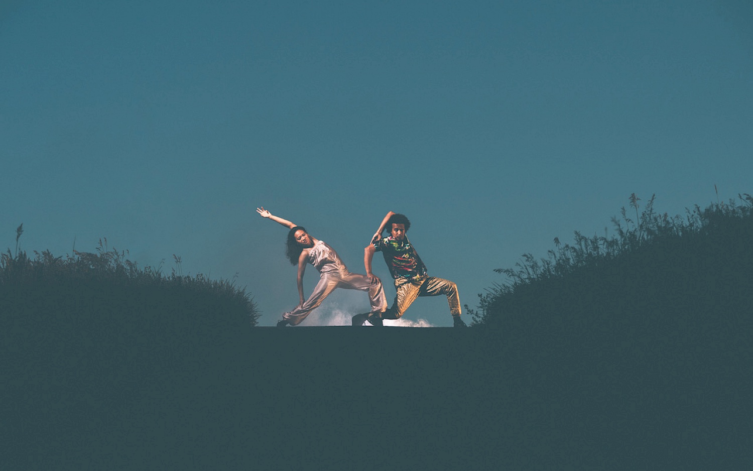 Raphael Moussa Hillebrand and Joy Alpuerto Ritter posieren in Tanzpose vor dem dunkelblauen Himmel.